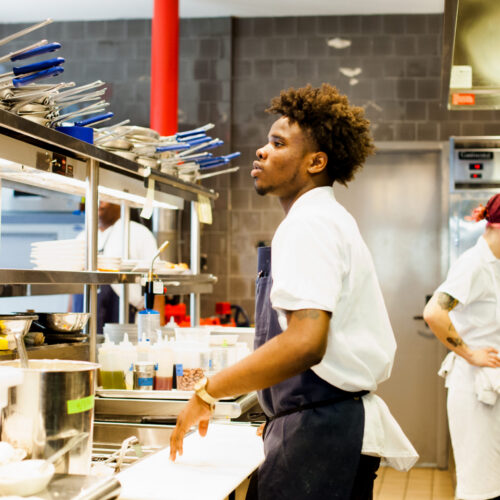Young person working in a professional kitchen as part of a culinary hospitality training program.