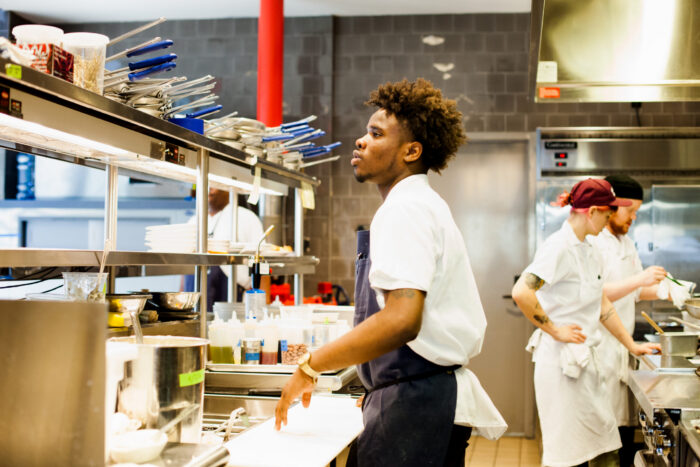 Young person working in a professional kitchen as part of a culinary hospitality training program.
